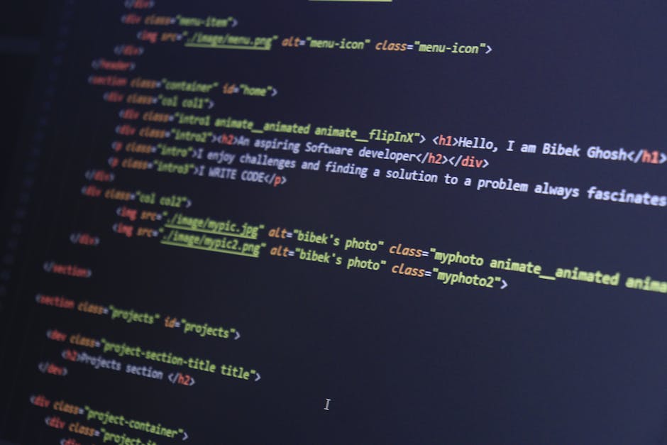 A close-up view of a person's hands typing on a small laptop or MacBook placed on a dark, reflective surface. The laptop's screen displays a coding environment with lines of multicolored code, includi